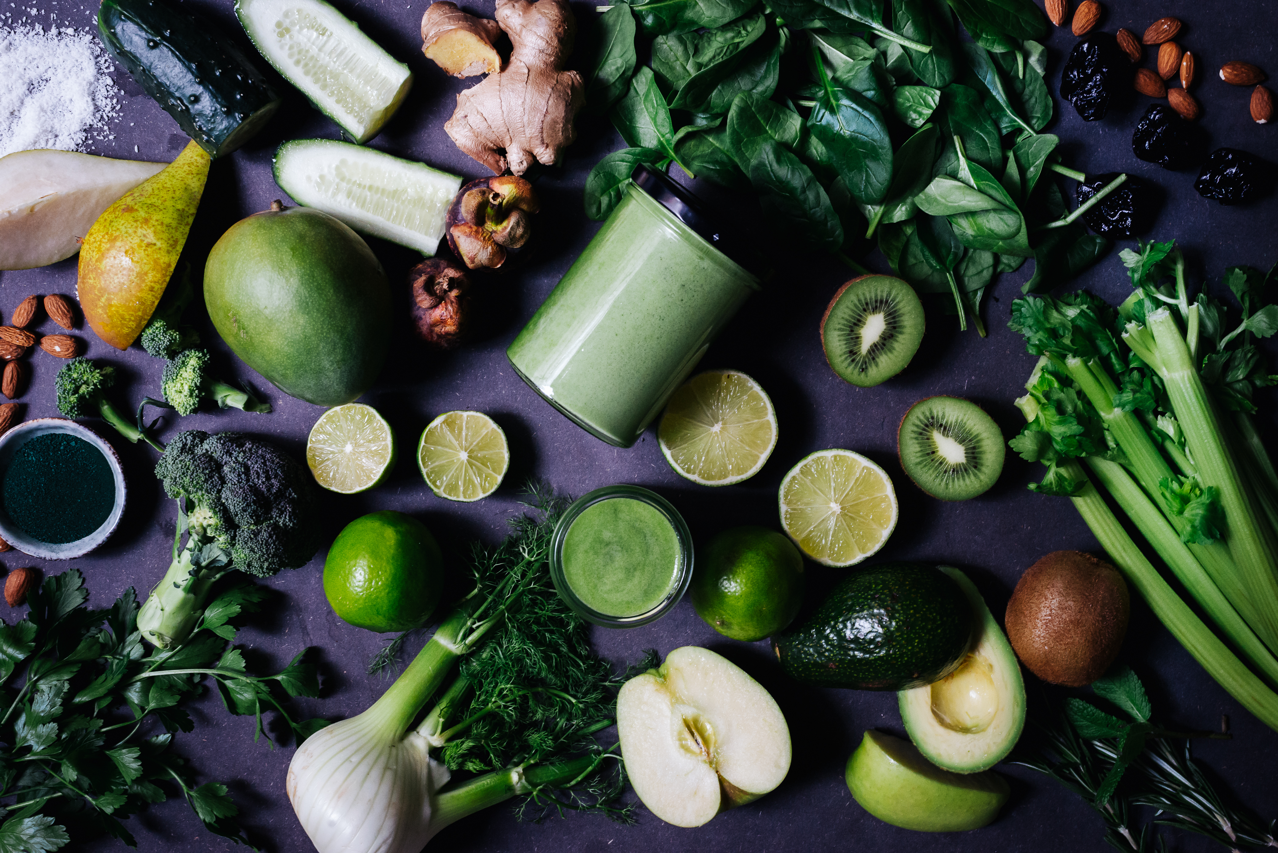 Grüner Smoothie im Glas umgeben von grünem Obst und Gemüse