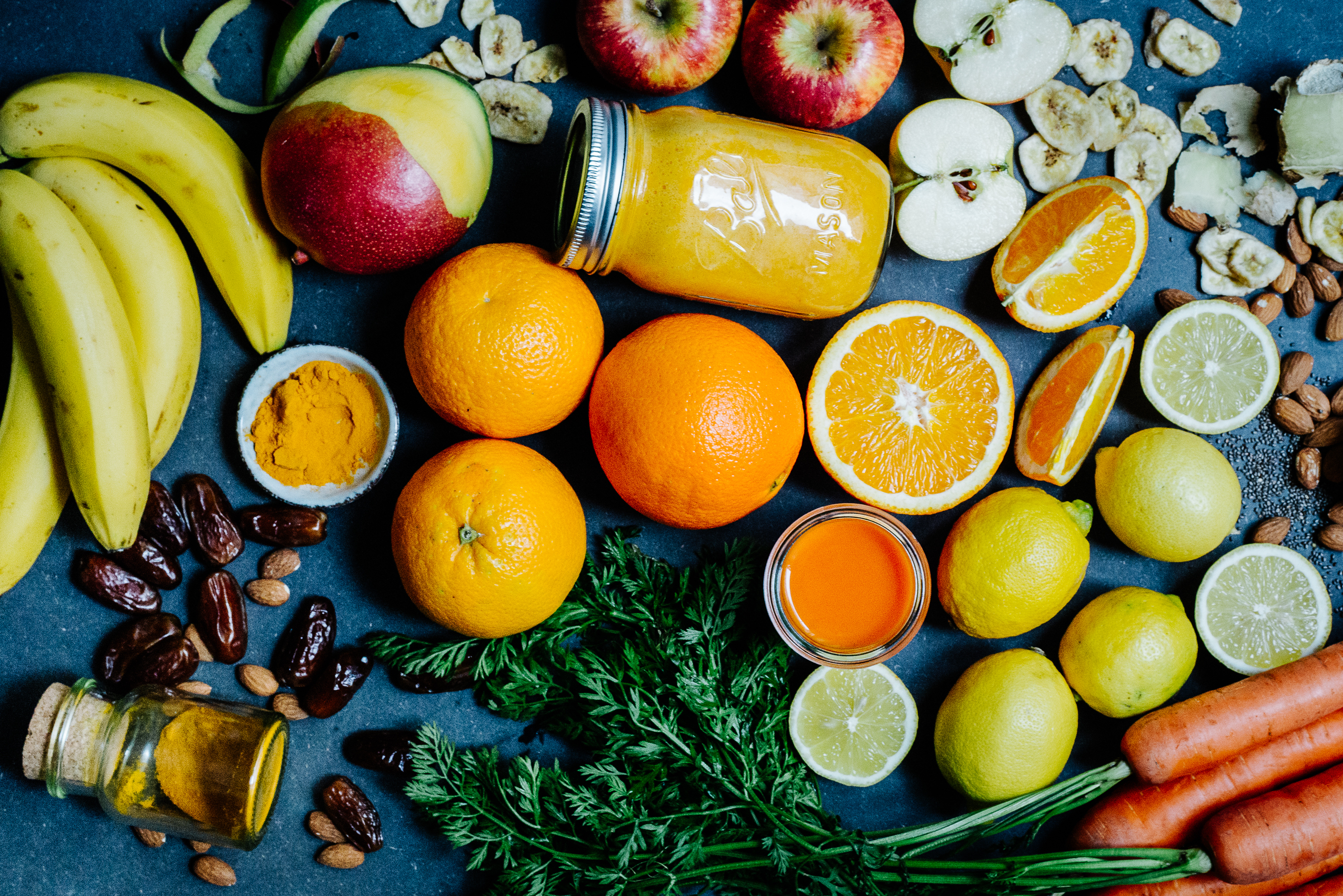 Gelber Smoothie umgeben von frischem Obst und Gemüse
