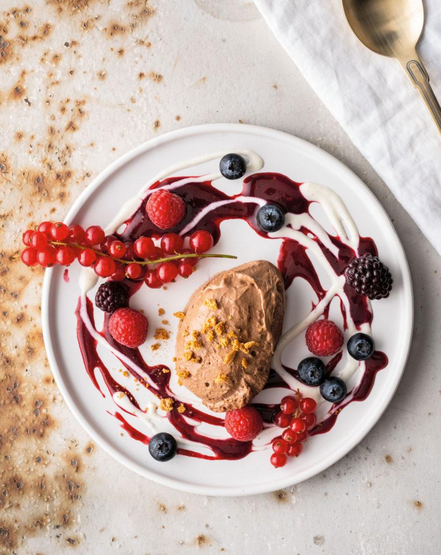 Schokoladenmousse mit Himbeeren, Heidelbeeren und Soße auf weißem Teller
